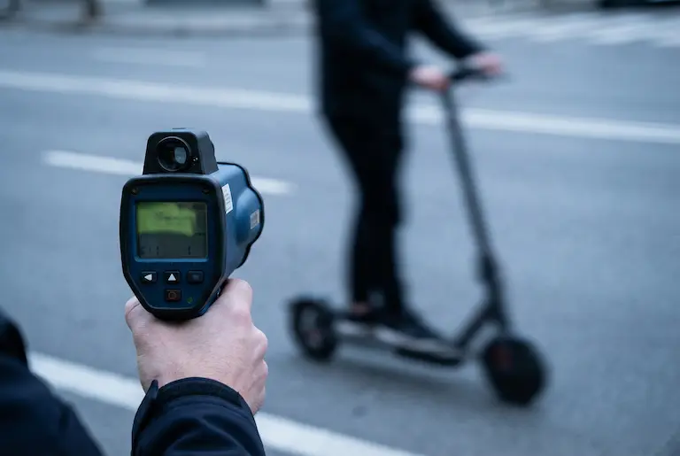 Primer pla d'un radar policial de velocitat apuntant a un patinet elèctric que circula amb excés de velocitat per una carretera.